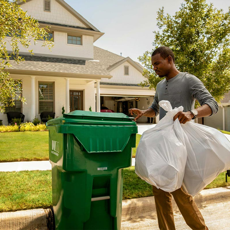 Man putting bags of trash into green WM trash container